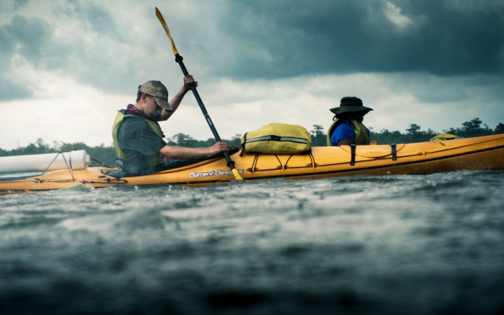 a young person works to paddle a kayak while it rains